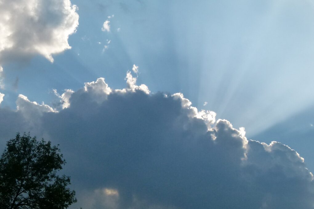 Blue sky with sunrays beaming out behind a gray cloud