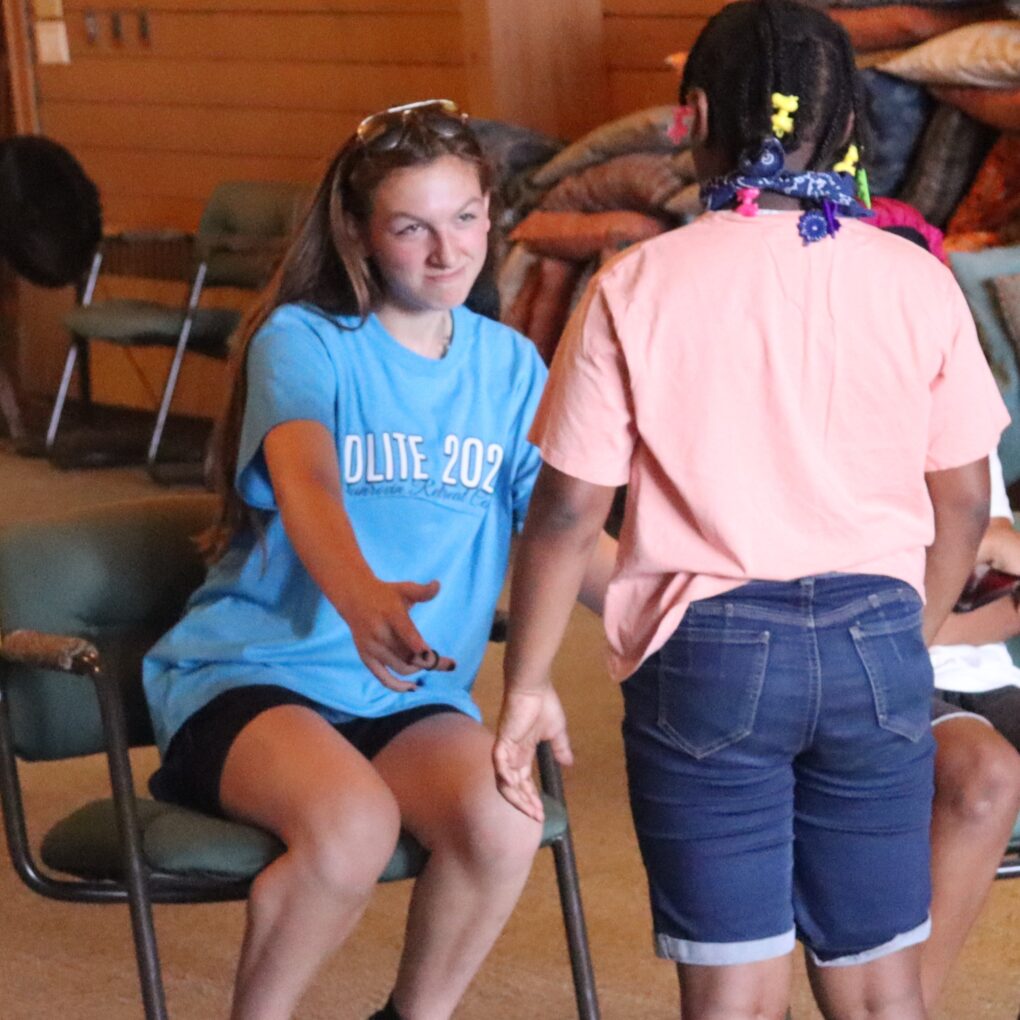 A high school teen reaching her hand out to a young girl