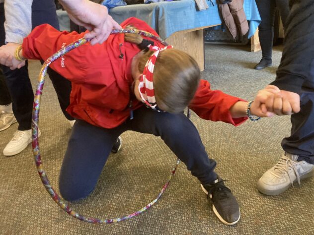 Blindfolded teenager in a red sweatshirt crawling through a hula hoop