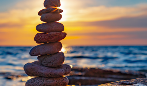 A rock cairn with a beautiful landscape of blue water and a sunrise in the background