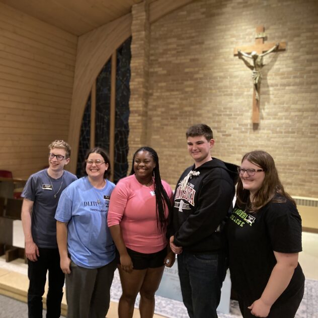Five young people in the Dunrovin Upper Room Chapel with the brick wall and hanging crucifix behind them