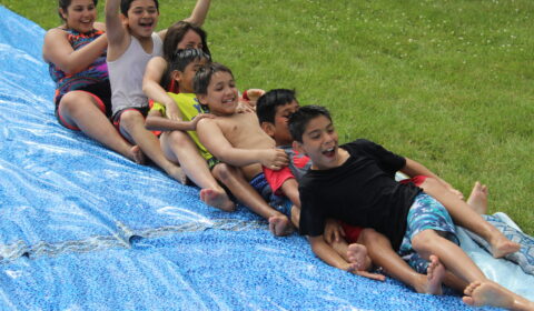 Boys going down the hill in a long train, on the Slip-N-Slide