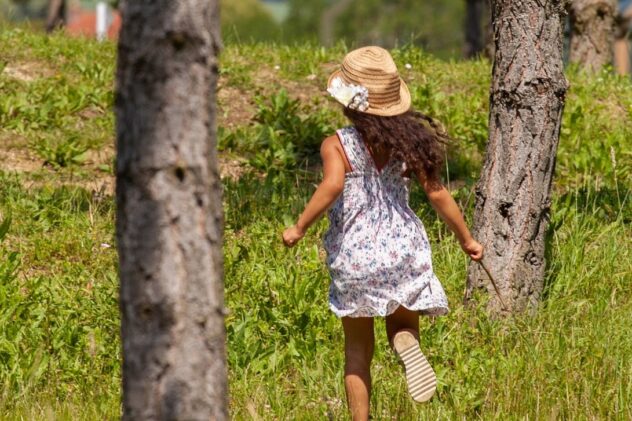 Little girl in a white and purple-flowered dress with a hat on running through the grass
