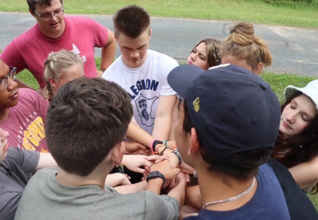 Several high school students with their hands all locked in the middle of a circle